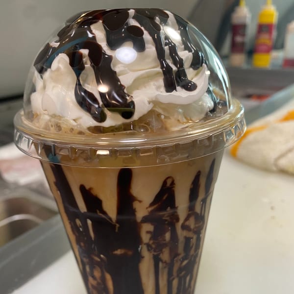 Iced coffee with whipped cream and chocolate drizzle in a clear plastic cup from 6th Street Deli.