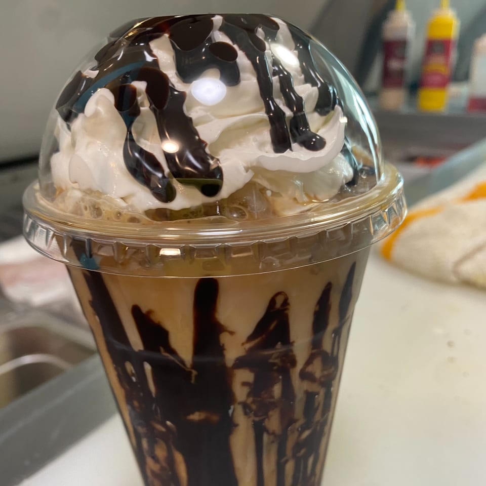Iced coffee with whipped cream and chocolate drizzle in a clear plastic cup from 6th Street Deli.