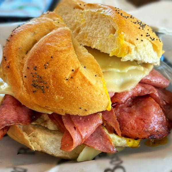 A deli sandwich with sliced meats, melted cheese, and mustard on a poppy seed bun.