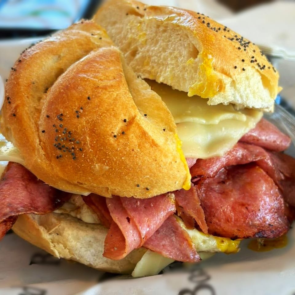 A deli sandwich with sliced meats, melted cheese, and mustard on a poppy seed bun.