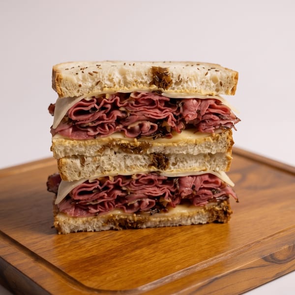 Tall pastrami sandwich with melted cheese and caramelized onions on seeded rye bread.