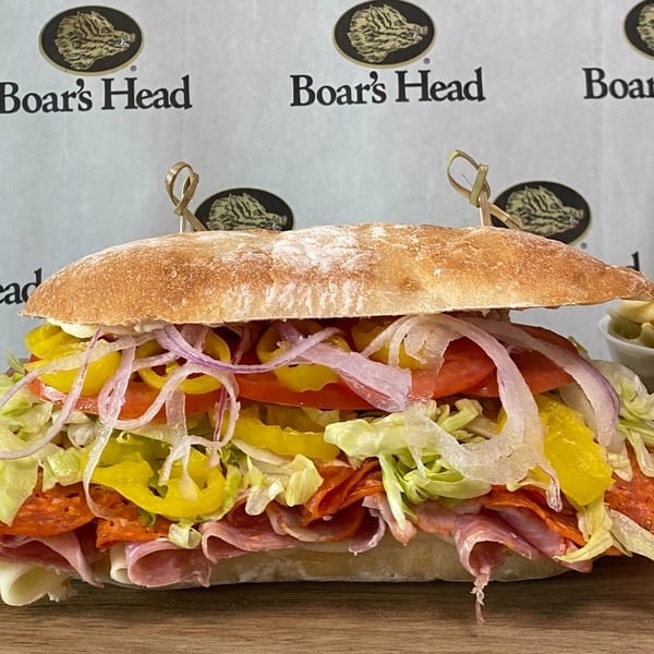 A large deli sub sandwich with various meats, cheese, lettuce, tomatoes, onions, and peppers.
